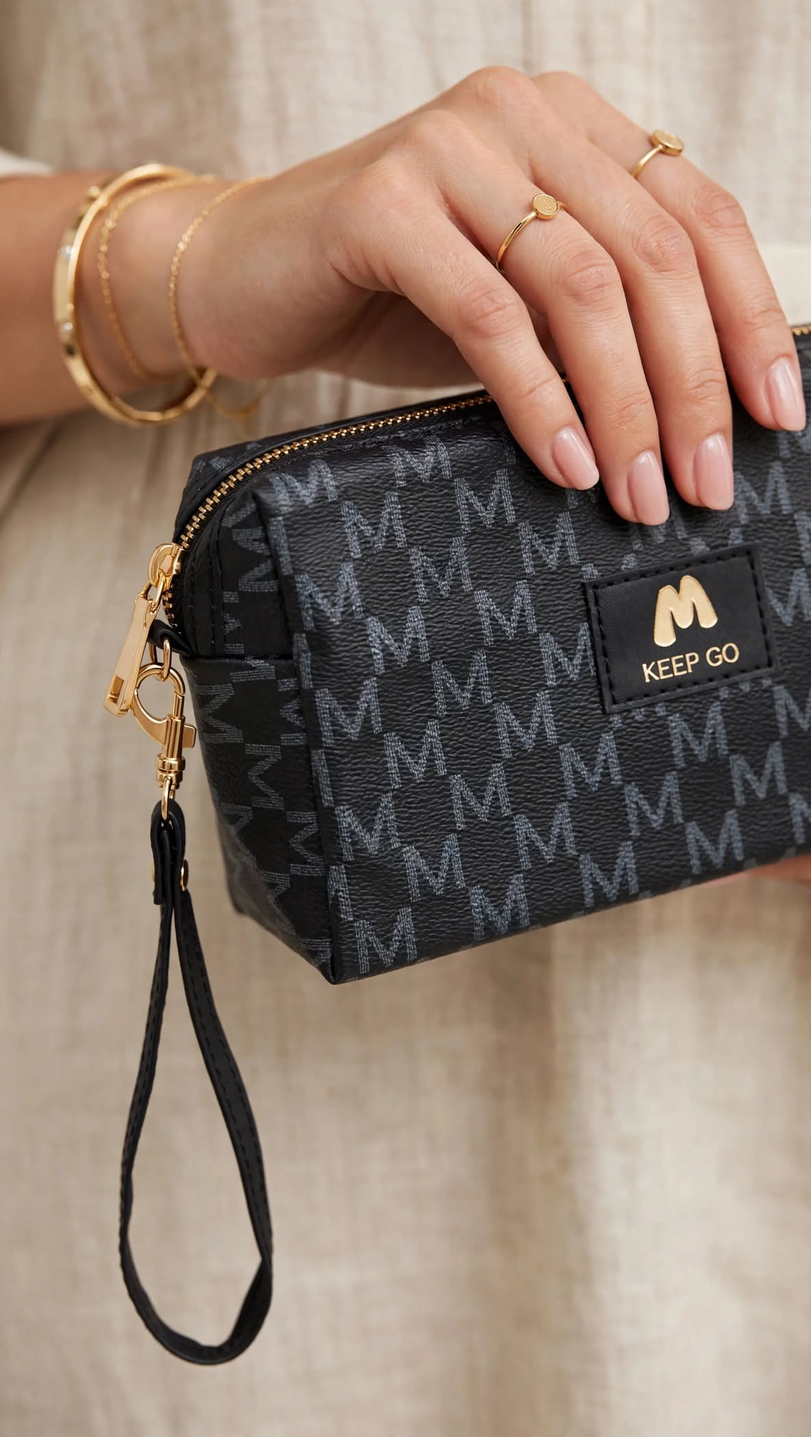 Woman holding Zorani black monogram wristlet pouch with gold hardware and wrist strap - luxury makeup pouch mini clutch for women Pakistan